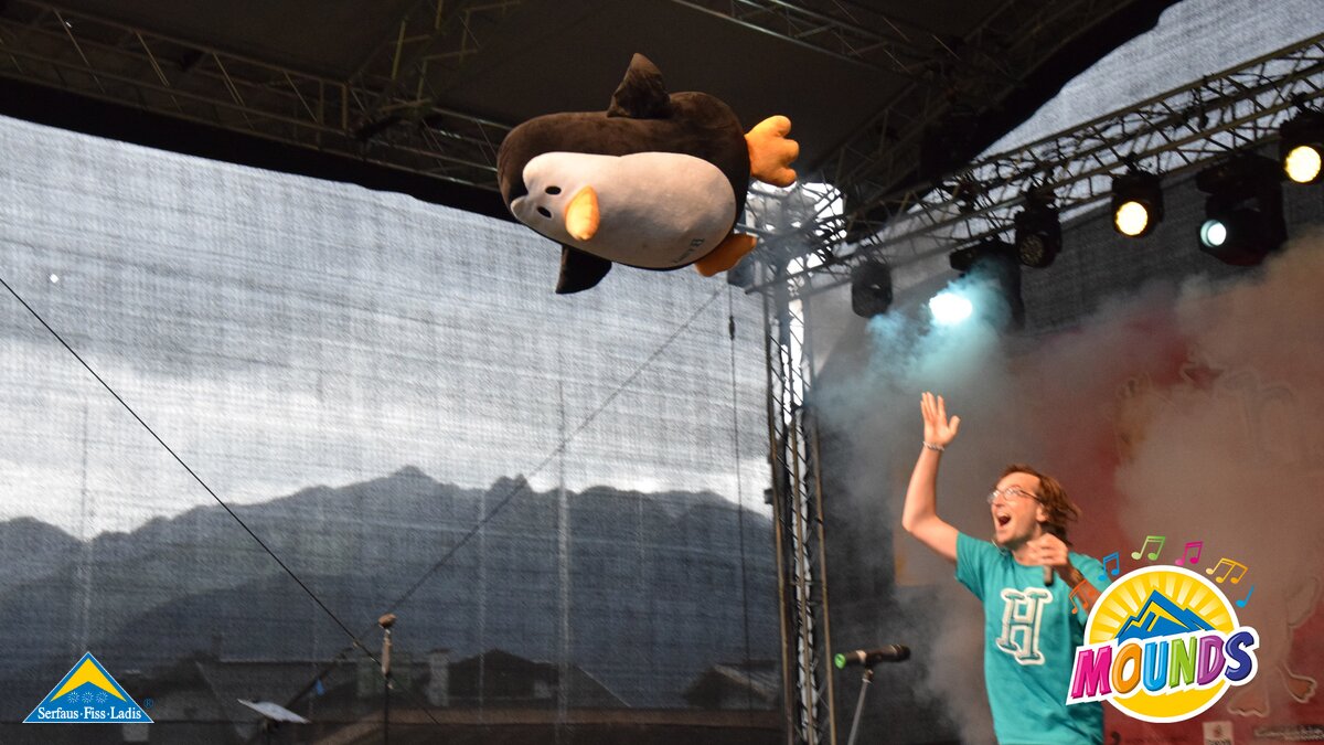 Der Pinguin fliegt Richtung Publikum | © Serfaus Fiss Ladis herrH wirft seinen Pinguin und dieser fliegt Richtung Publikum vor der MOUNDS Festivalbühne in Serfaus Fiss Ladis in Tirol | © Serfaus Fiss Ladis