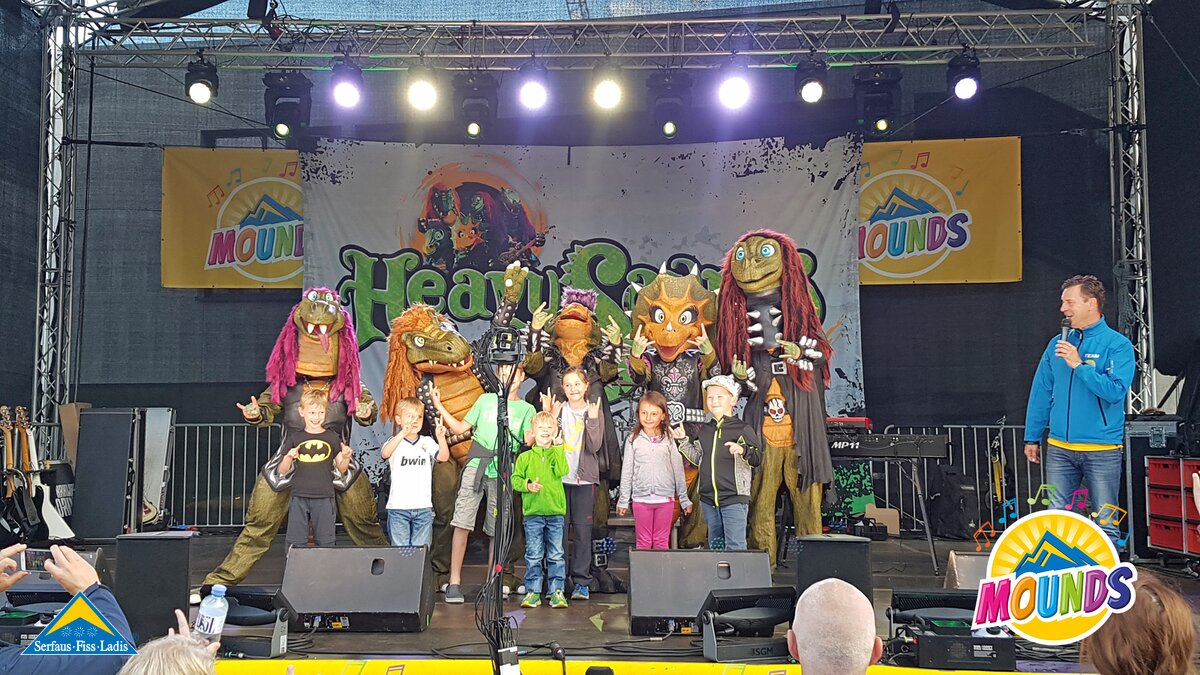 Heavysaurus mit Kindern | © Serfaus Fiss Ladis Heavysaurus mit Kindern auf der Festivalbühne von MOUNDS - Dem Musikfestival für die ganze Familie in Serfaus Fiss Ladis in Tirol | © Serfaus Fiss Ladis