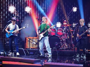 Vier Jungs spielen auf der Bühne Musik mit Gitarren und Schlagzeug.