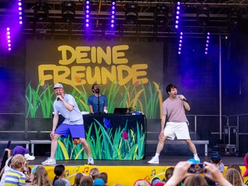 Zwei Moderatoren performen Musik auf einer Kinderveranstaltung.