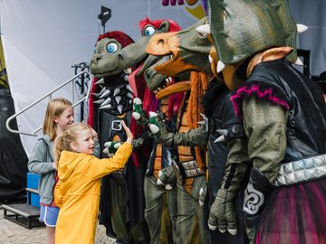 Zwei Mädchen interagieren mit Drachen-Maskottchen auf Fest.