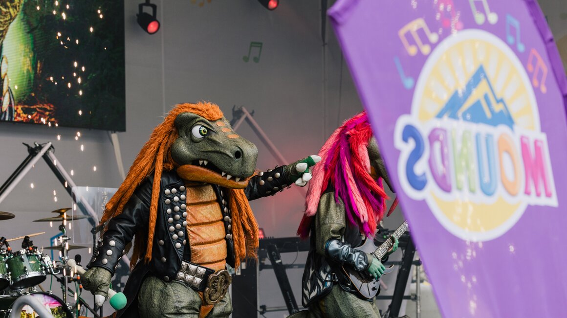 Dinosaurier-Maskottchen bei Live-Auftritt auf der Bühne.