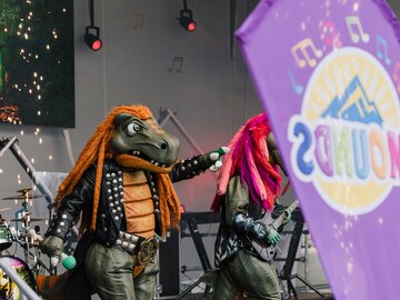 Dinosaurier-Maskottchen bei Live-Auftritt auf der Bühne.