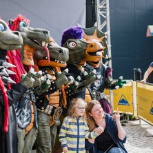 Familie posiert mit kostümierten Drachen-Figuren auf einer Veranstaltung.