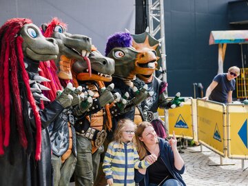 Familie posiert mit kostümierten Drachen-Figuren auf einer Veranstaltung.