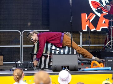 Ein Künstler liegt auf einem Klavier und entertaint das Publikum.