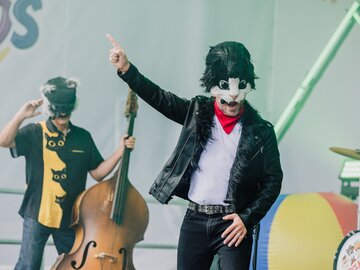 Zwei Musiker in Katzenmasken bei einem Auftritt, einer singt, der andere spielt Kontrabass.