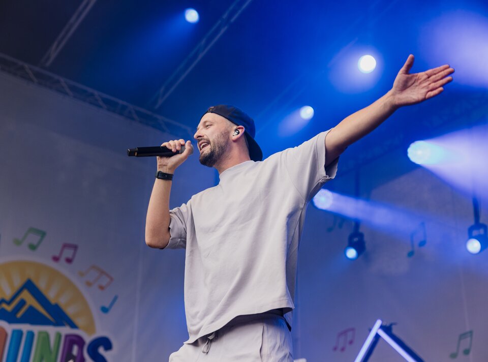 Ein Sänger auf der Bühne mit Mikrofon, im Hintergrund Musiknoten.