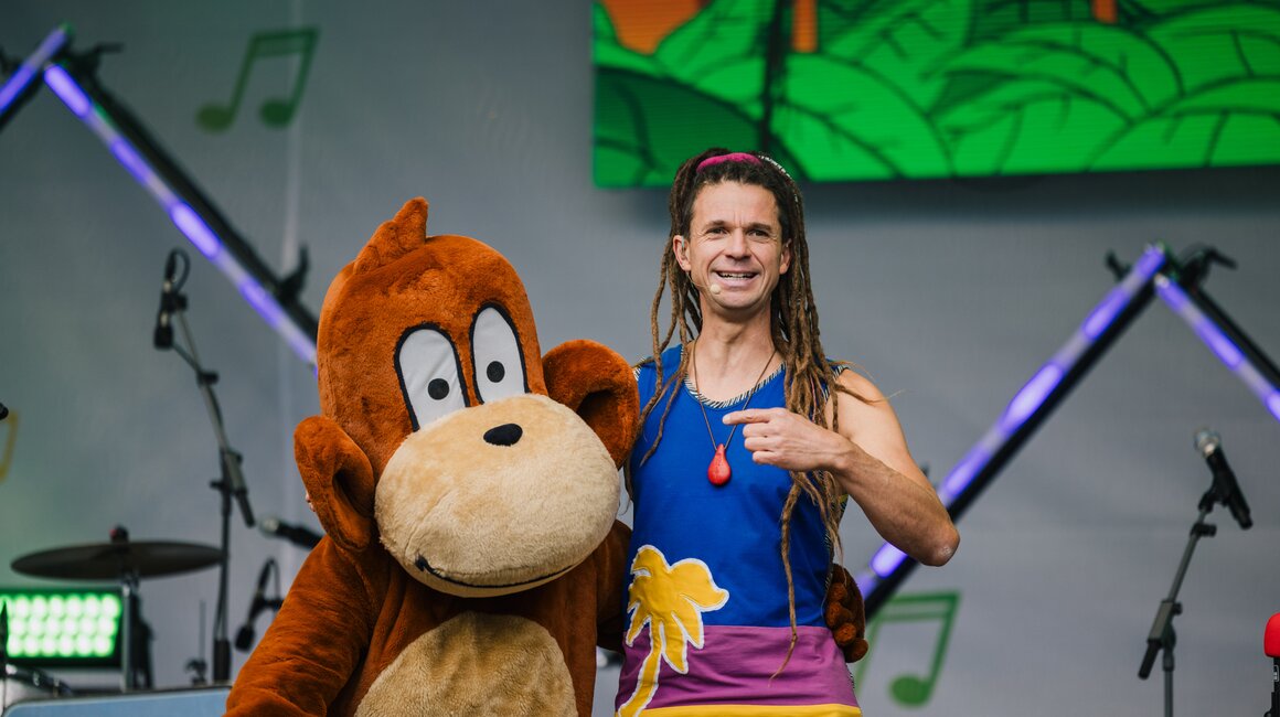 Ein Mann mit Dreadlocks zeigt auf Diddy Kong bei einem Auftritt.