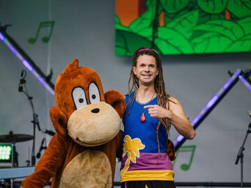 Ein Mann mit Dreadlocks zeigt auf Diddy Kong bei einem Auftritt.