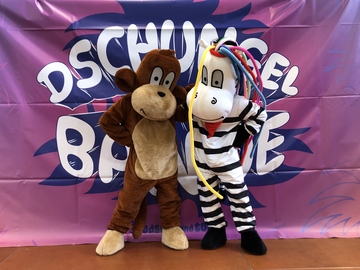 Zwei Maskottchen posieren vor einem bunten Dschungel-Backdrop.