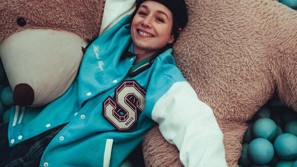 Ein lächelndes Kind umarmt einen großen Teddybär in einem Raum voller blauer Bälle.