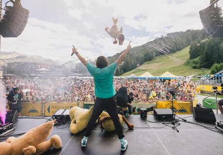 Ein Musiker steht auf der Bühne und wirft Kuscheltiere ins Publikum.