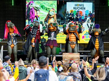 Drachen-Maskottchen tanzen auf einer Bühne vor Publikum.