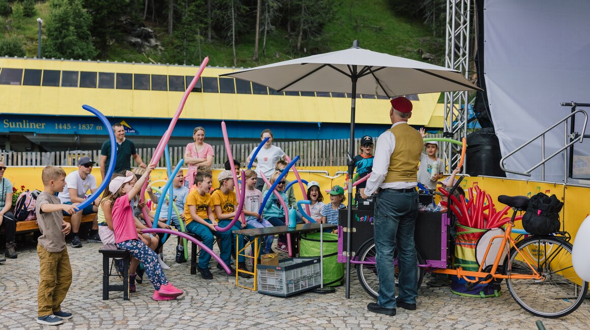 Eine Gruppe Kinder mit Luftballons hört einem Animateur zu.
