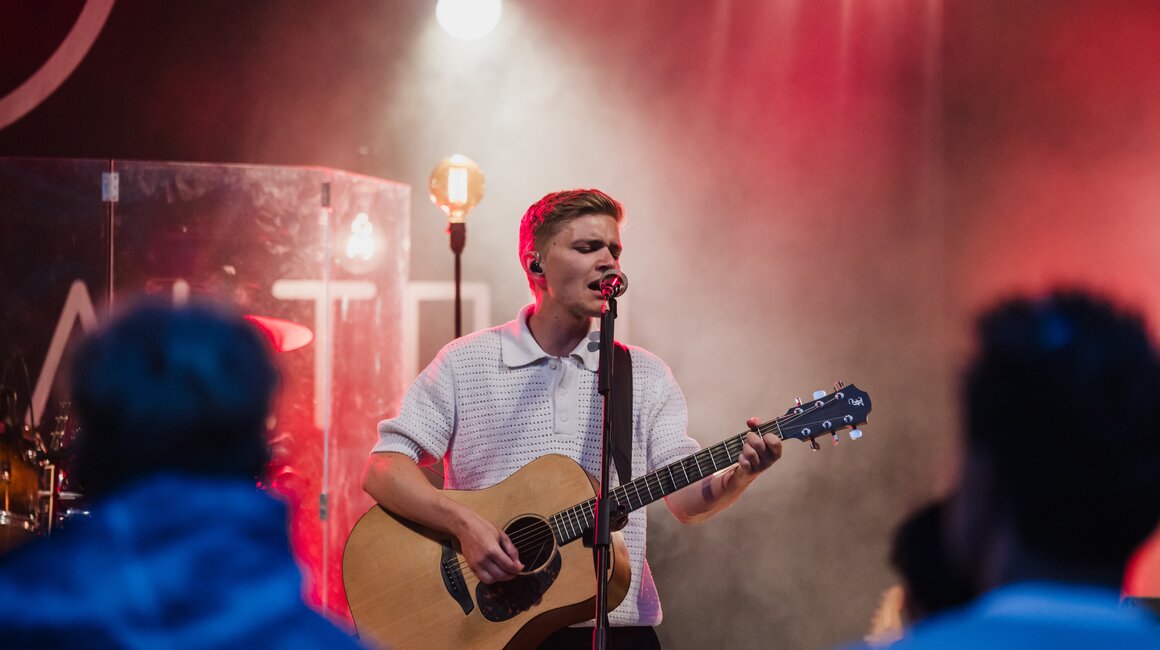 Junger Musiker performt live mit Akustikgitarre auf einer Bühne.