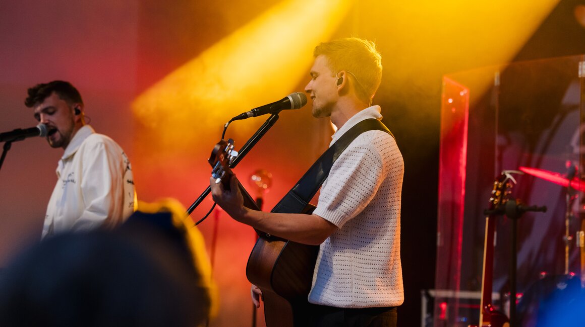 Zwei Musiker treten live auf, einer spielt Gitarre und singt.