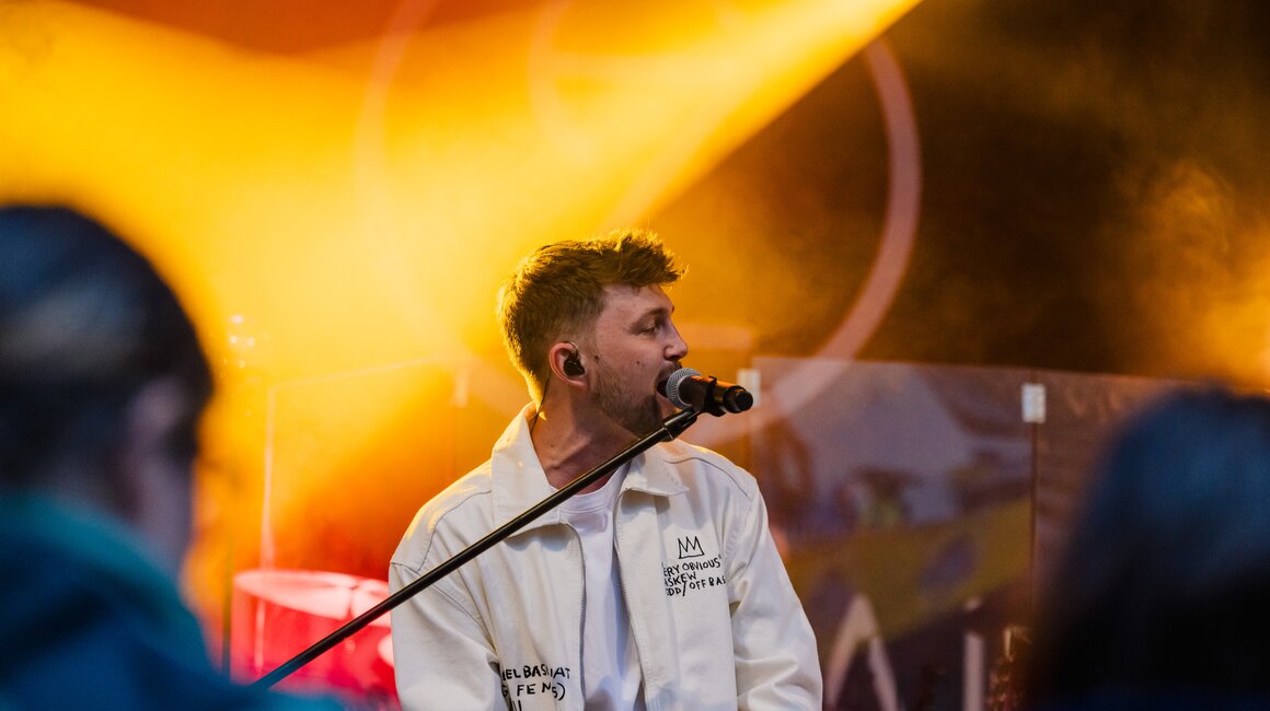 Ein junger Mann singt auf der Bühne mit Mikrofon und in einem weißen Jacket.