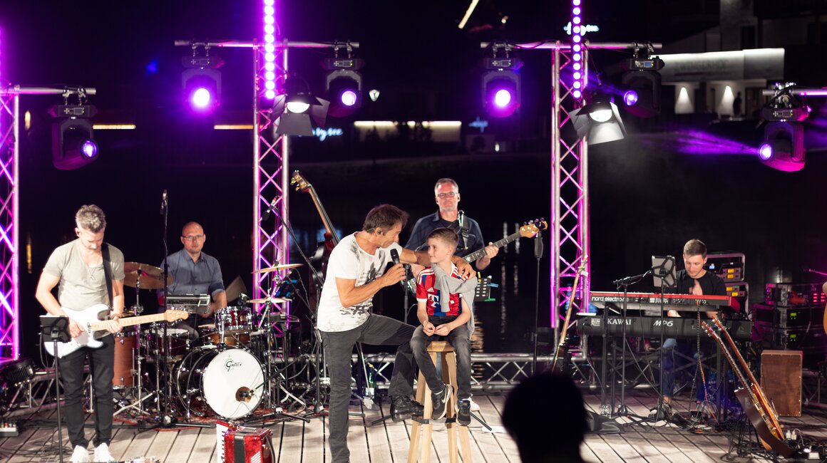 Musiker singt mit einem Jungen auf der Bühne bei einem Konzert.