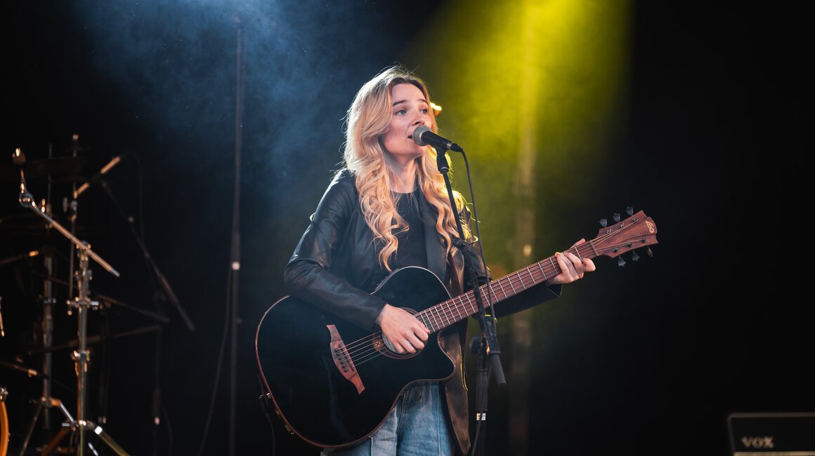 Eine blonde Sängerin spielt Gitarre und singt live.