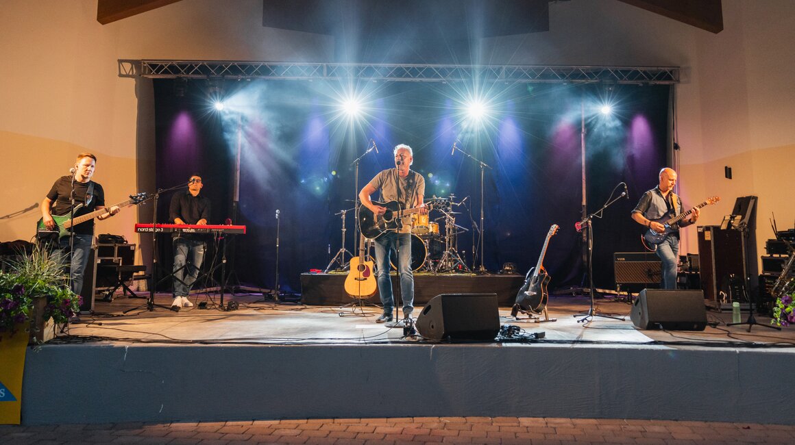 Eine Band spielt live auf einer Bühne mit Lichtern und Instrumenten.