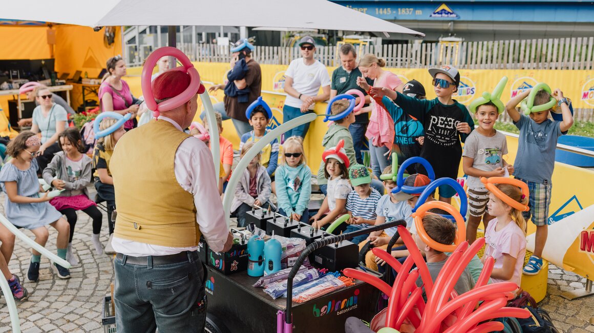 Ein Ballonkünstler zeigt Kindern verschiedene Ballonformen bei einem Event.