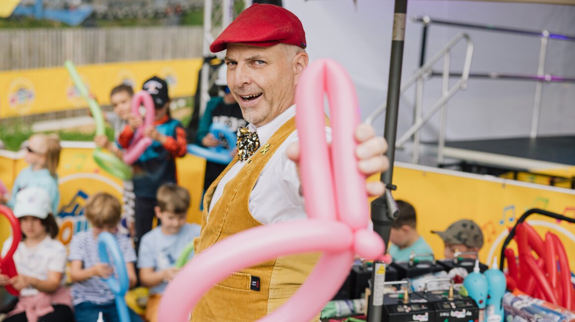 Ein Unterhaltungskünstler zeigt ein Ballontier vor einer Kinderschar.